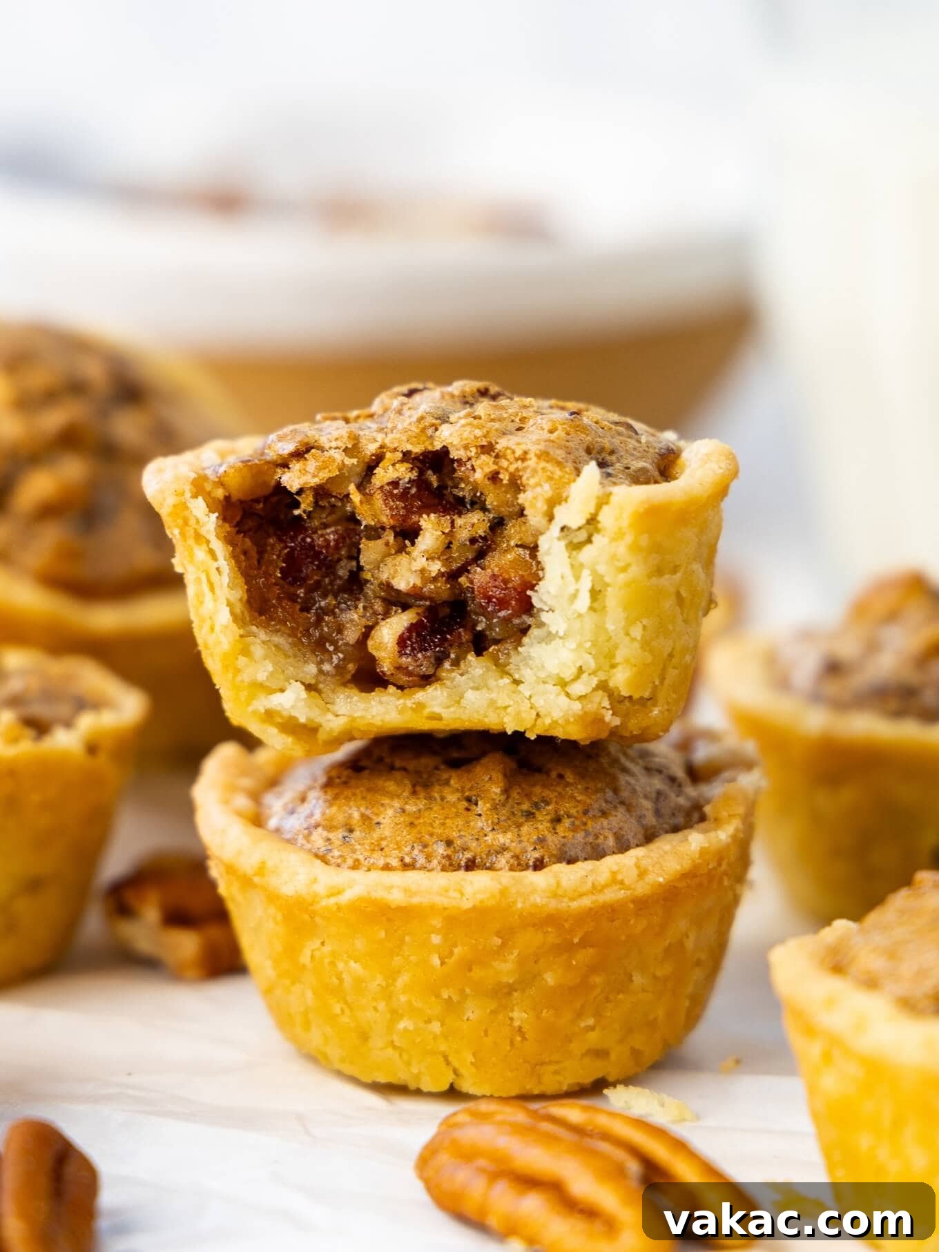 Southern Pecan Treasures 9 Two perfectly baked pecan tassies stacked, with the top one showing a small bite taken, revealing the gooey, nutty interior.