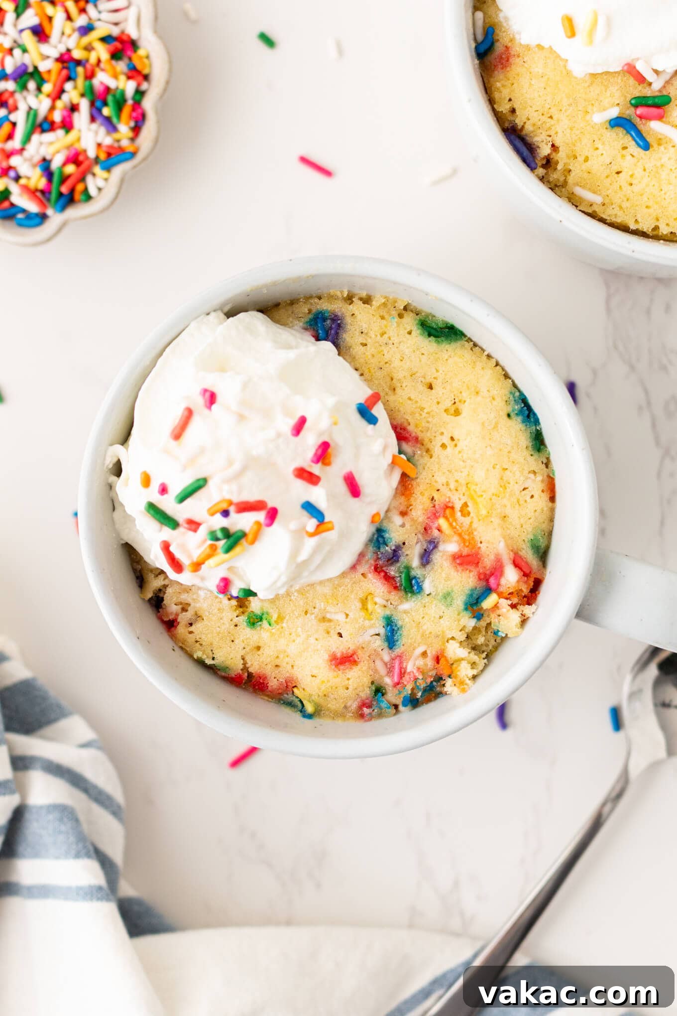 Cozy Vanilla Mug Treat 2 A beautifully garnished vanilla mug cake, seen from an overhead perspective, topped with fluffy whipped cream and a hint of a spoonful, ready to be enjoyed.