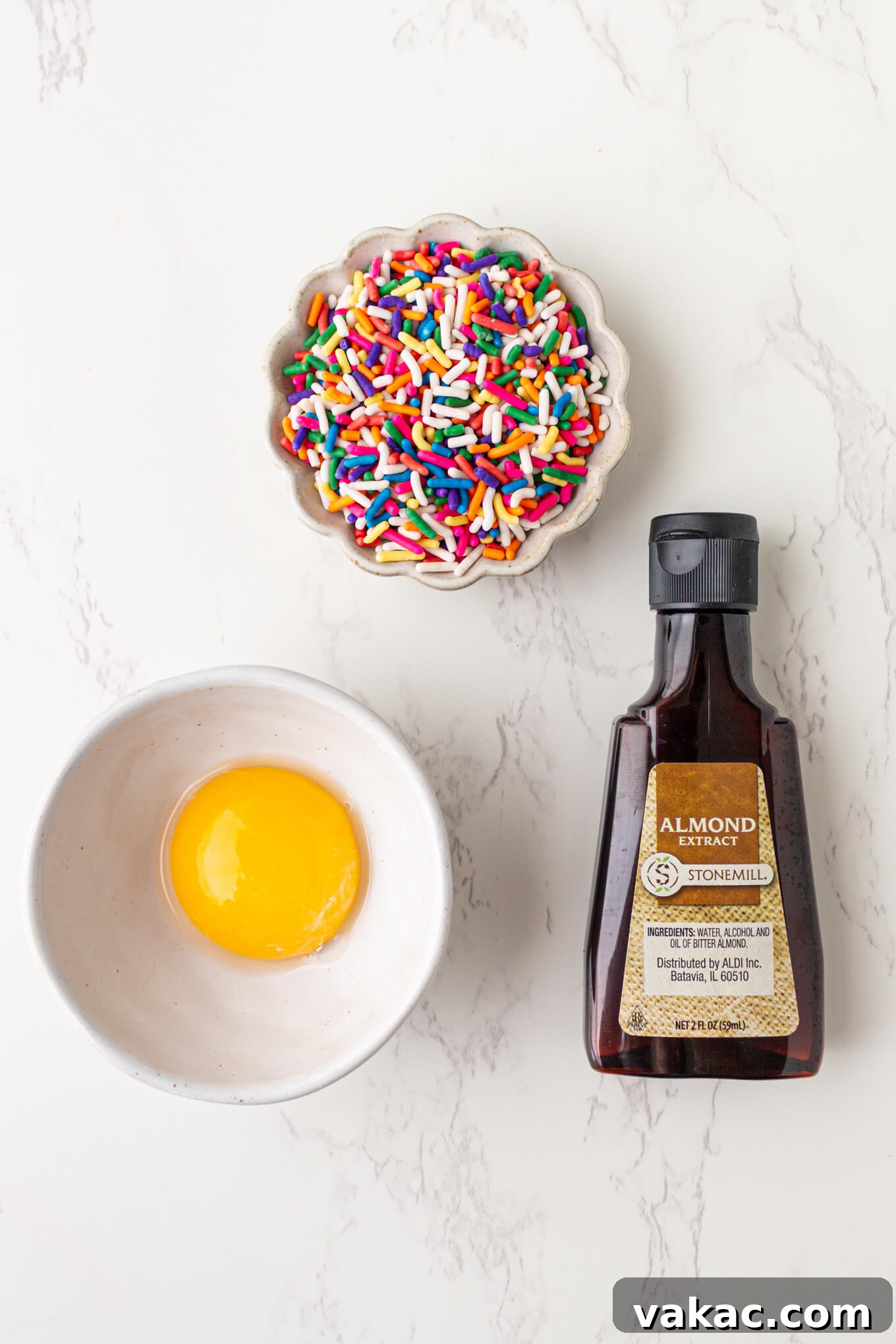 Cozy Vanilla Mug Treat 3 An overhead shot showcasing key ingredients for a vanilla mug cake: a vibrant egg yolk, a small bottle of almond extract, and a scattering of colorful rainbow sprinkles.