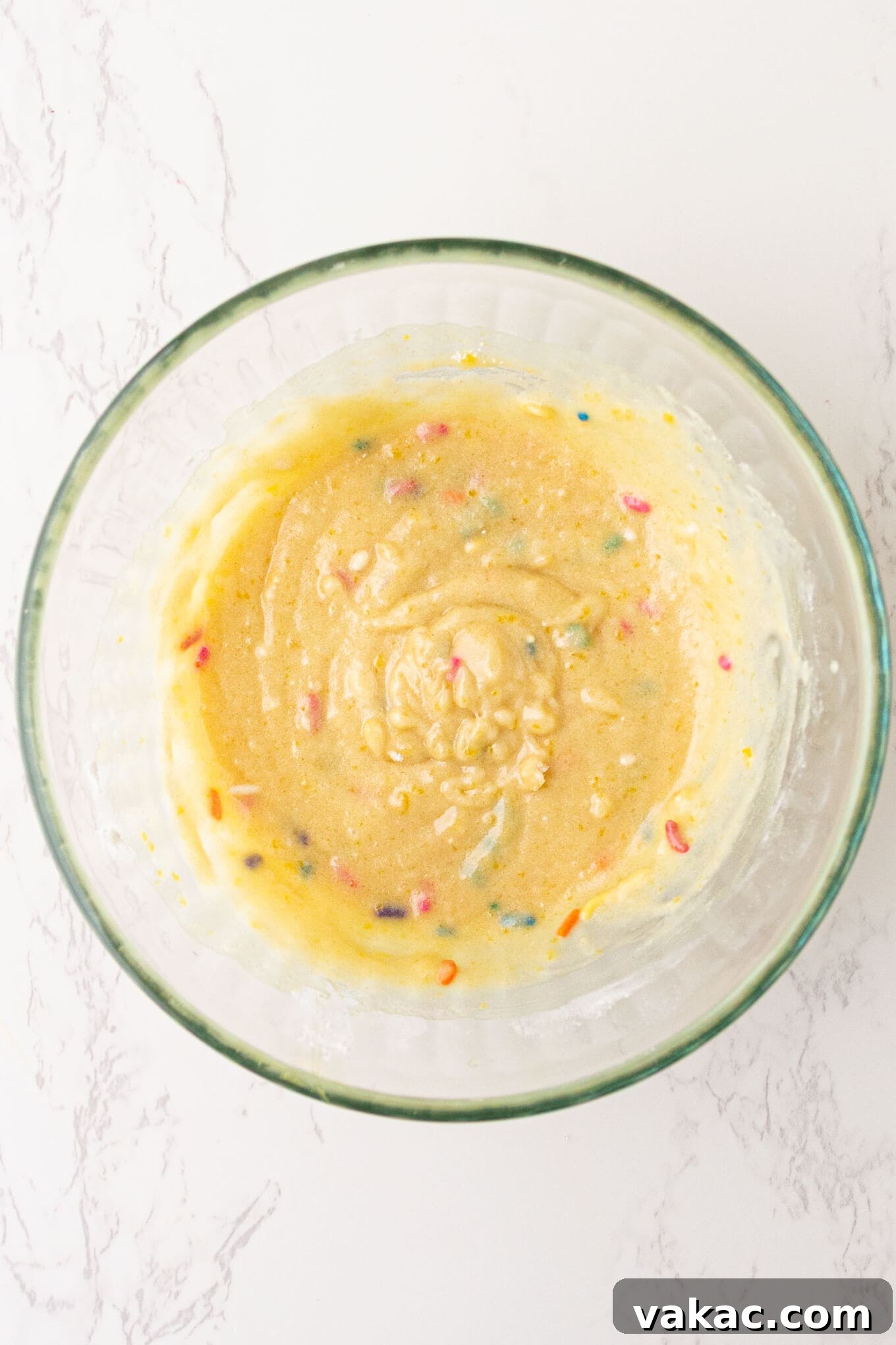 Cozy Vanilla Mug Treat 4 Smooth, creamy vanilla cake batter expertly mixed in a clear glass bowl, ready for baking.