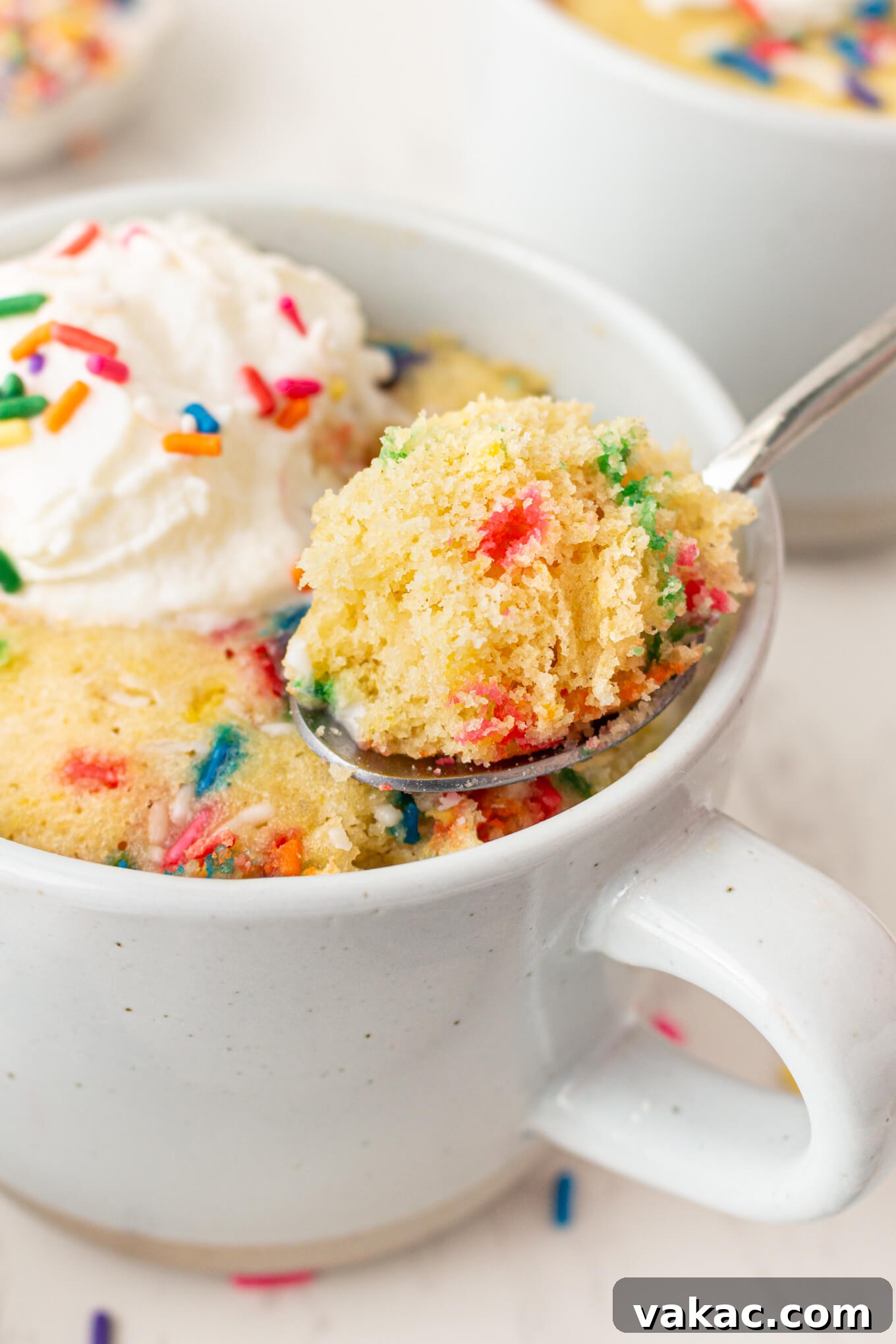 Cozy Vanilla Mug Treat 7 A small spoonful of light vanilla cake resting delicately on the rim of a ceramic mug, highlighting the cake's soft texture and inviting warmth.