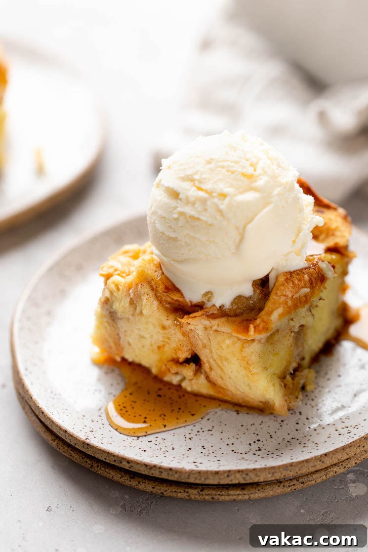 Grandma's Legacy Bread Pudding 2 A slice of bread pudding topped with a scoop of ice cream on a white speckled plate, highlighting its comforting appeal.