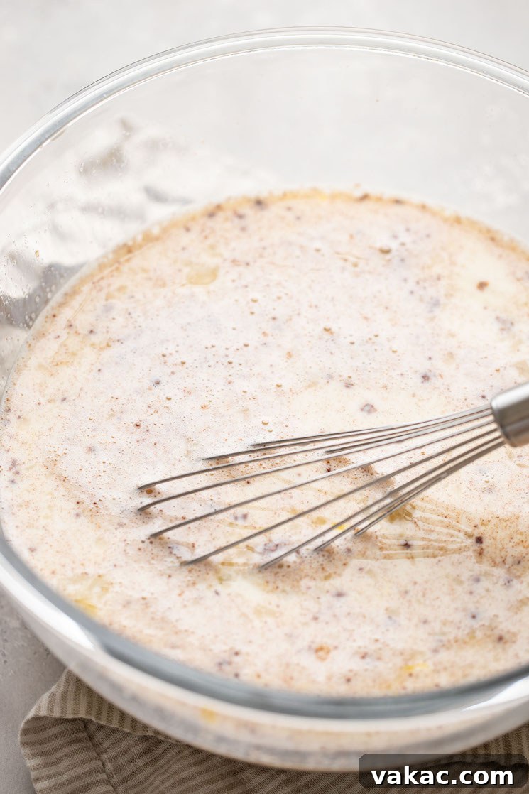 The creamy custard mixture being whisked together in a clear glass bowl, showing its smooth consistency.