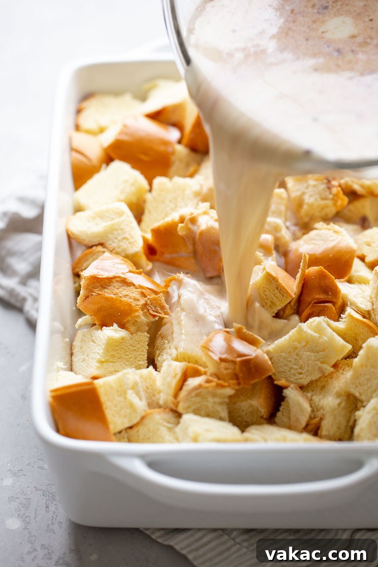 The luscious egg custard mixture being poured over cubed bread in a 9x13 pan, showing even distribution.