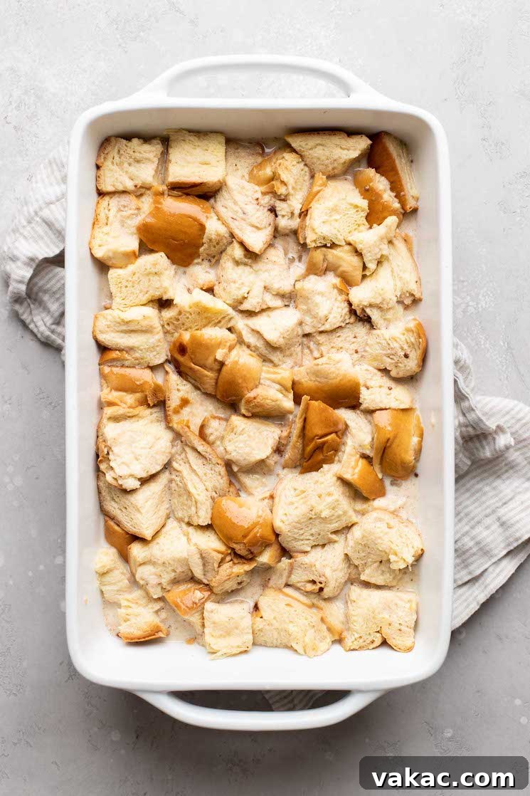 A pan of bread pudding soaking up the custard before baking, showing the bread fully submerged.