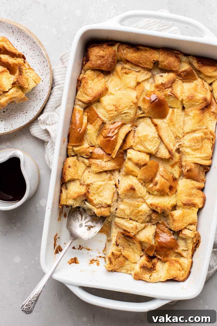 Grandma's Legacy Bread Pudding 8 An overhead view of golden-brown bread pudding in a 9x13 pan, with a perfect slice and a small container of syrup beside it.