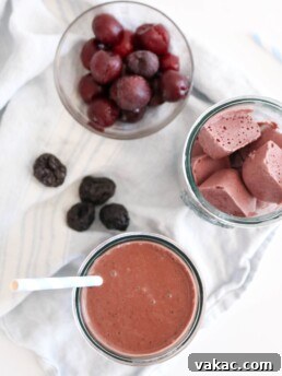 A photo of a dark chocolate cherry prune smoothie on a white food photography board with white kitchen towels and some prunes placed around it.