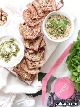A white serving plate filled with crackers with dip placed beside them. This image is associated with the Inspired Greens Superfood Pesto recipe.