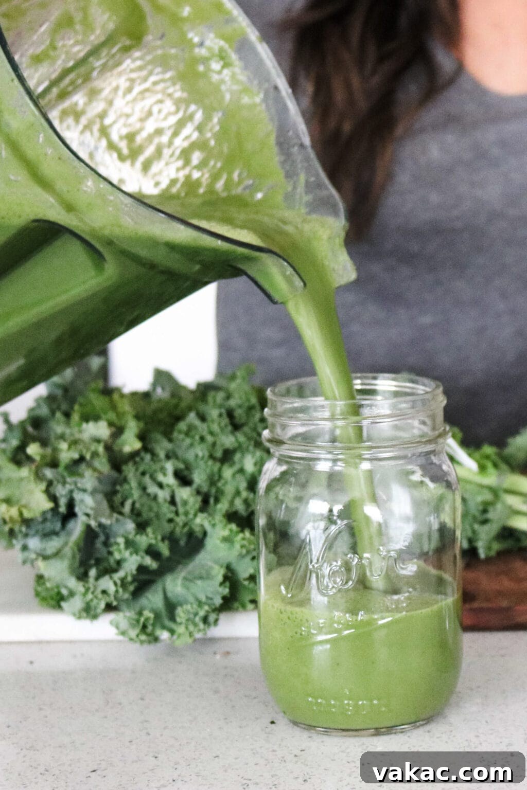 A Vitamix blender smoothly pouring freshly made green juice into a mason jar, with a rustic cutting board and vibrant curly kale in the background, highlighting the ease of preparation.