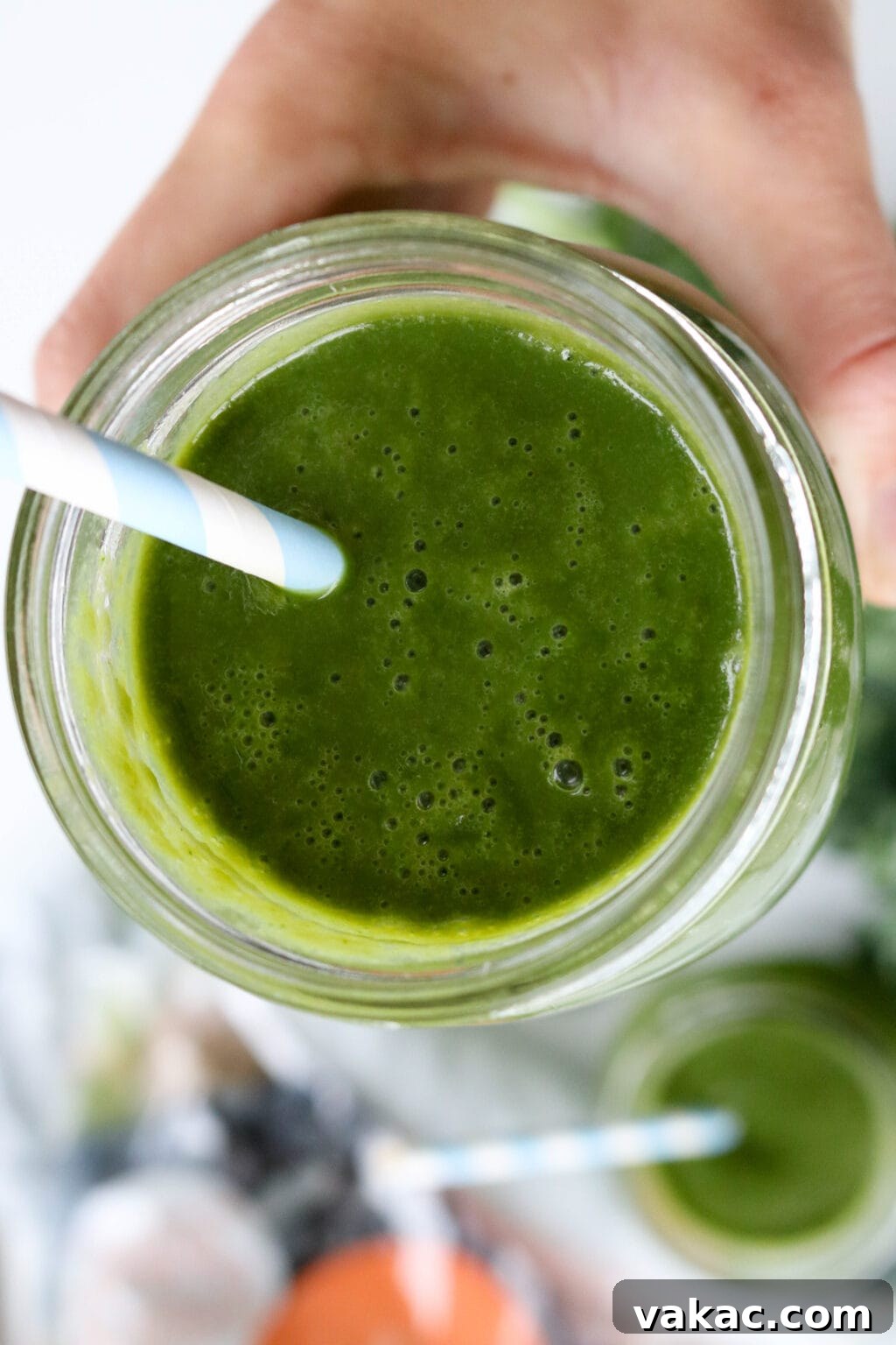 A woman's hand gracefully holding a mason jar filled with the vibrant, freshly made green juice, ready to be enjoyed.