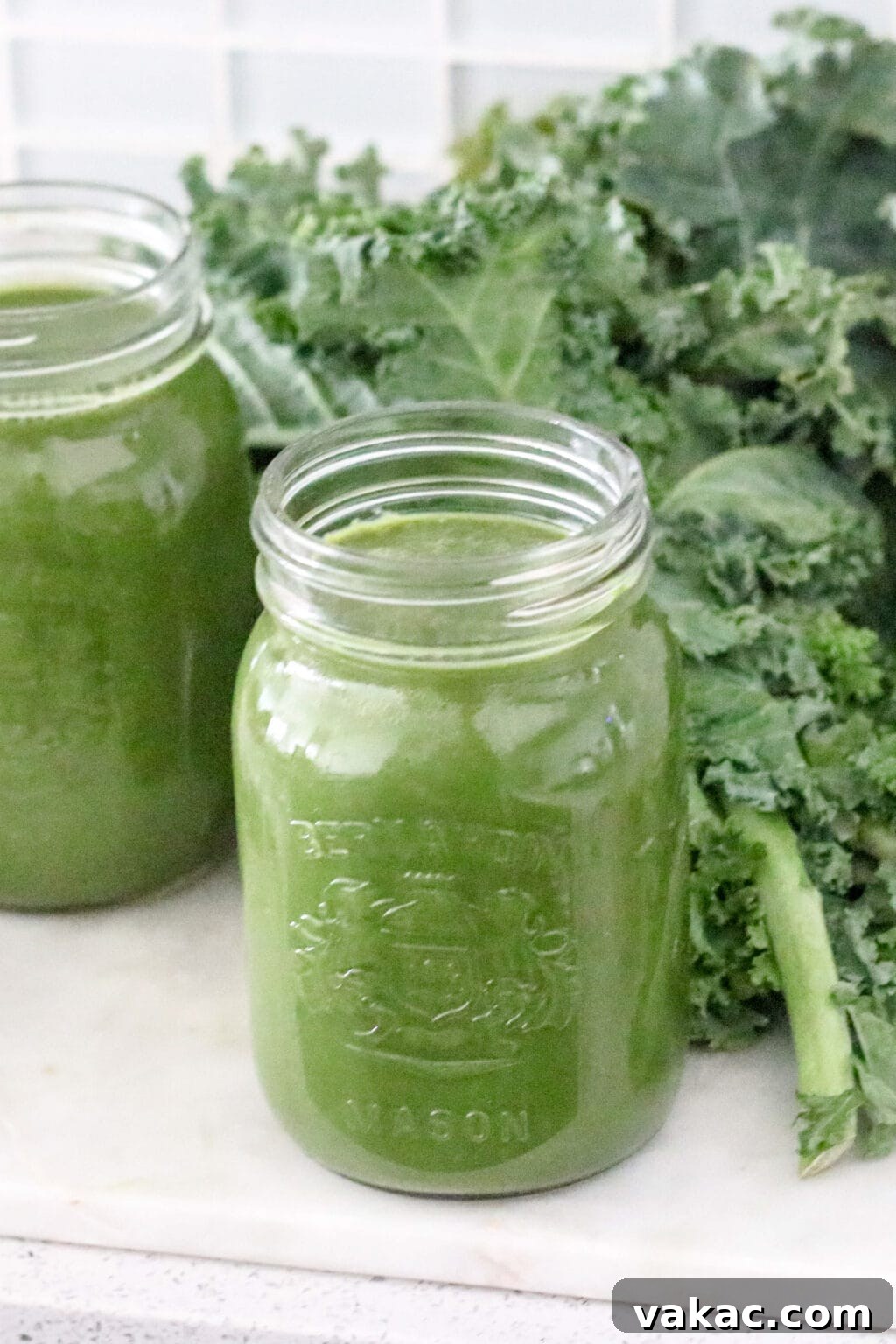 Two elegant mason jars filled with the vibrant green juice, resting on a clean counter, with fresh curly kale artfully arranged in the background, ready to be served.