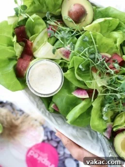 A white plate filled with greens and a small bowl of creamy Greek salad dressing.