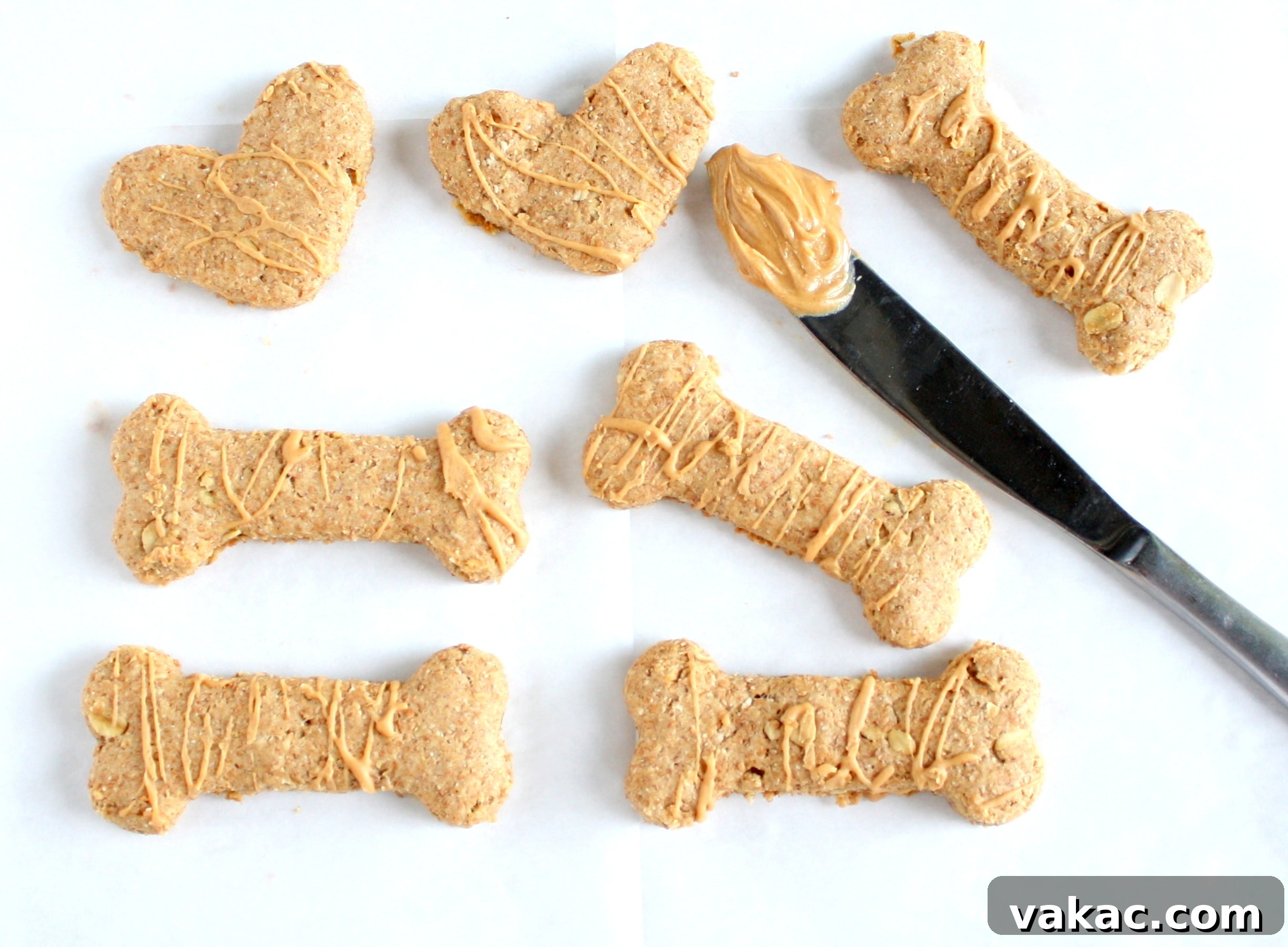 Overhead view of homemade peanut butter dog treats in various shapes. A knife with peanut butter on it rests in the middle.