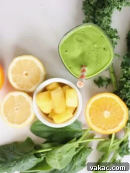Ingredients for a green smoothie recipe for pregnancy laid out on a white cutting board. Ingredients include kale, avocado, coconut milk, greek yogurt, mango, orange, lemon, mint, ginger