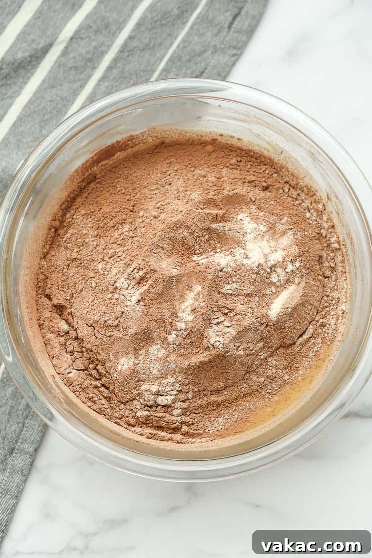 A clear bowl filled with the wet ingredients for homemade brownies, topped with the sifted dry ingredients before mixing.
