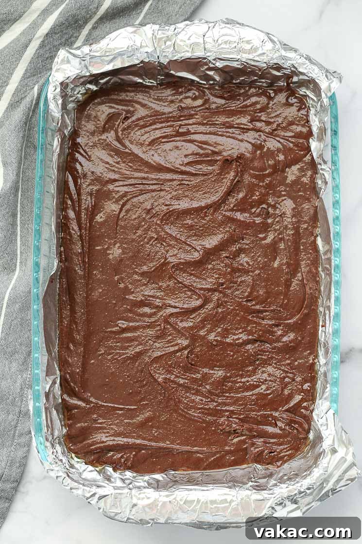 Fudgy Homemade Brownie Delights 4 A clear baking pan lined with aluminum foil, filled with evenly spread homemade brownie batter.