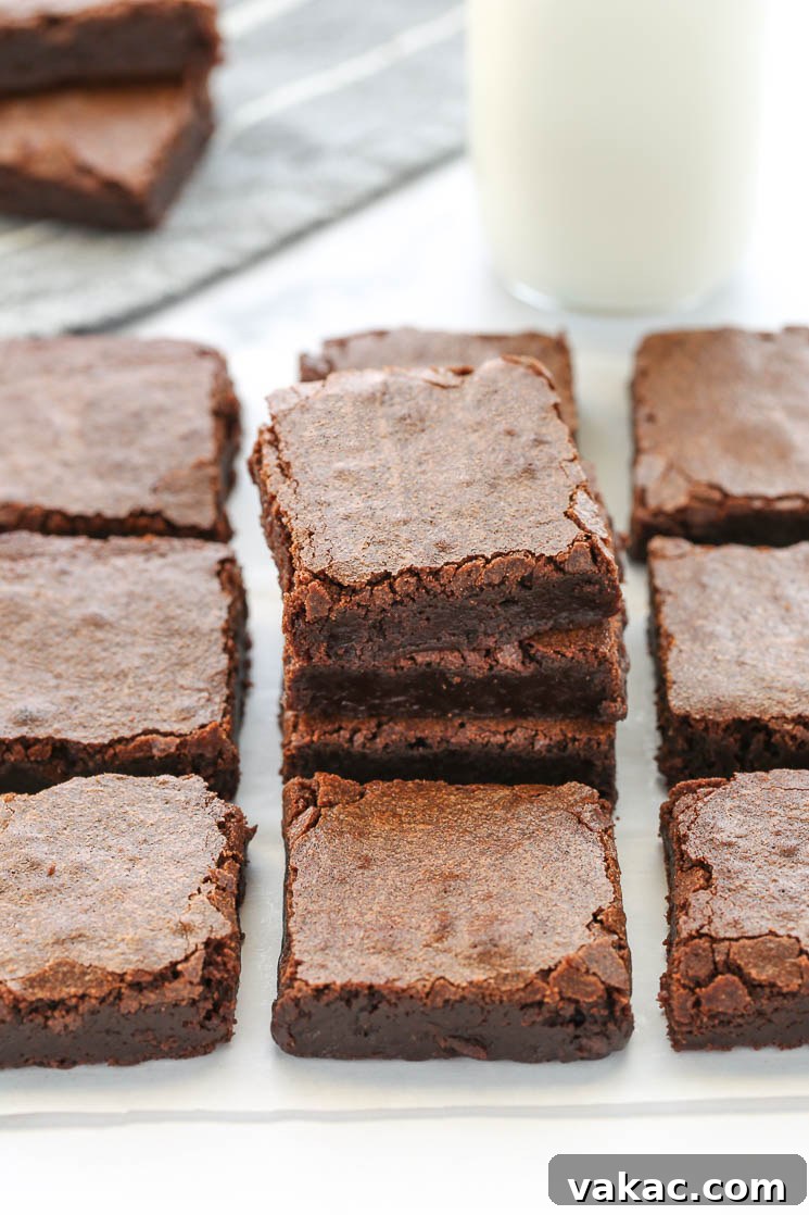 Fudgy Homemade Brownie Delights 5 A stack of sliced fudgy brownies, with more brownies, a glass of milk, and additional brownies in the background.