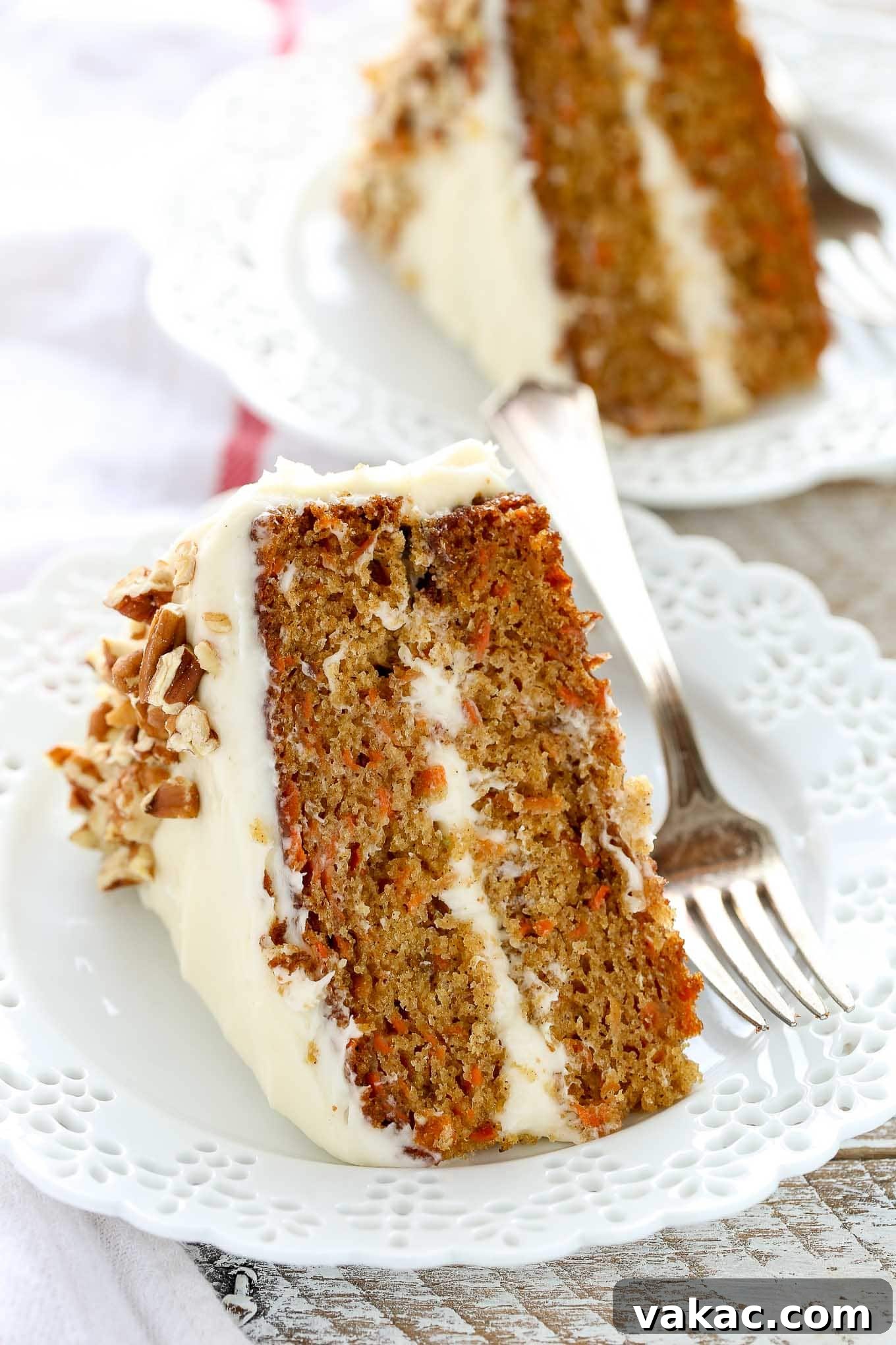 Two slices of carrot cake on separate decorative white plates. A fork rests on the side of each plate.