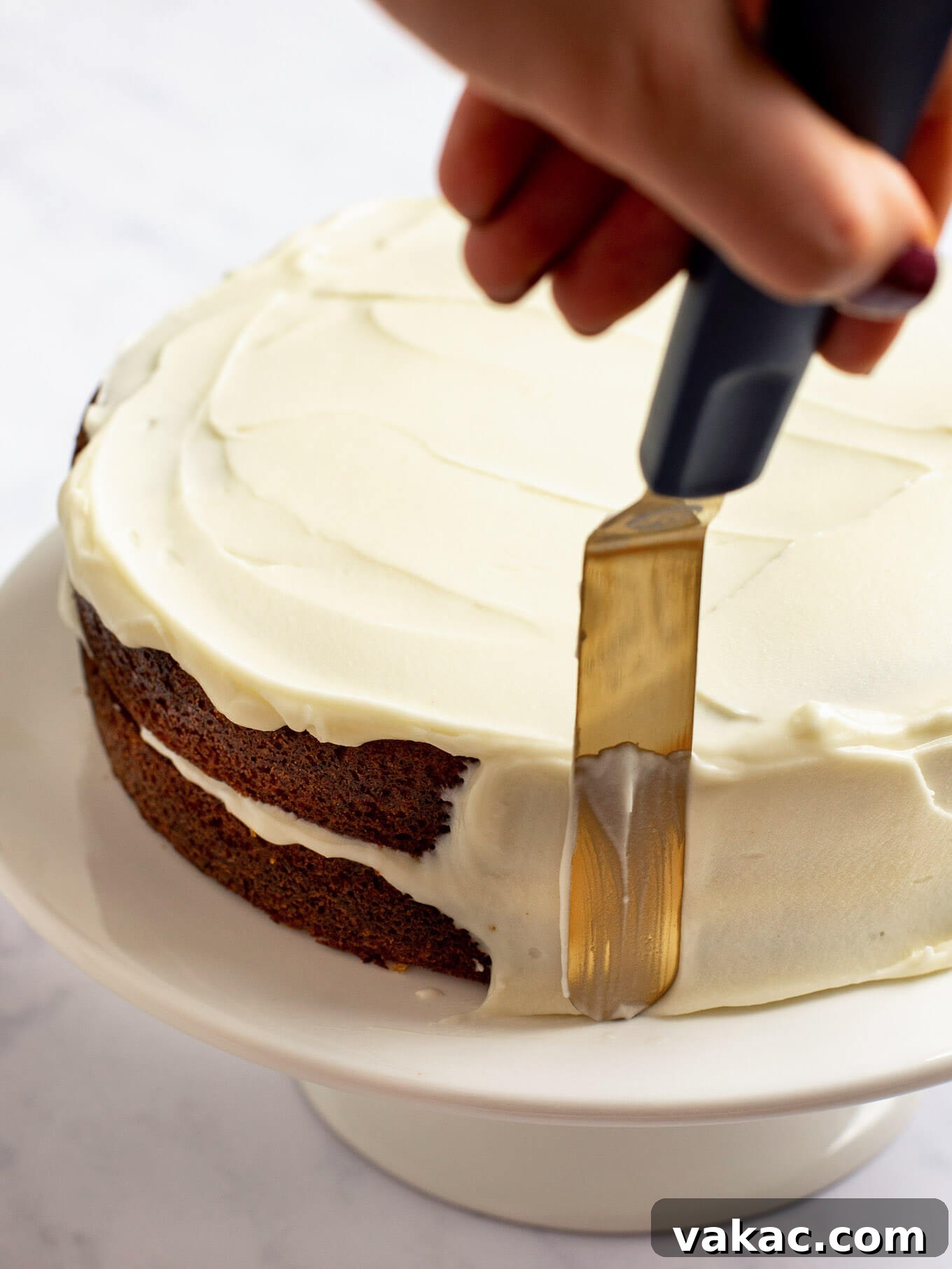 A carrot cake being frosted on the top and sides with cream cheese frosting.