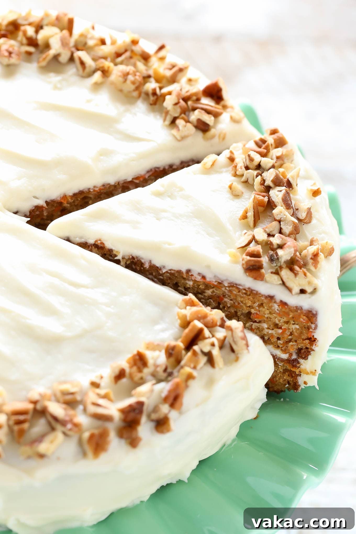 A carrot cake assembled on a green cake stand topped with cream cheese frosting and chopped pecans.