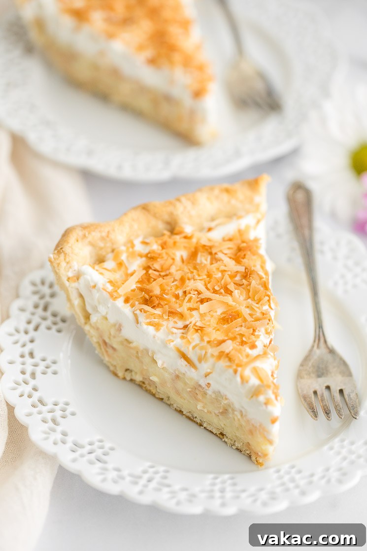 A slice of coconut cream pie on a decorative white plate with another slice in the background.