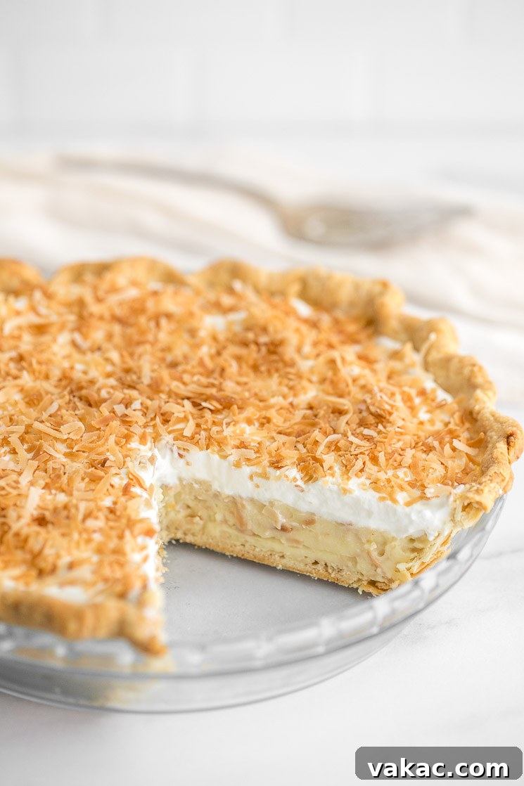 A close-up of a coconut cream pie with a slice taken out of it.
