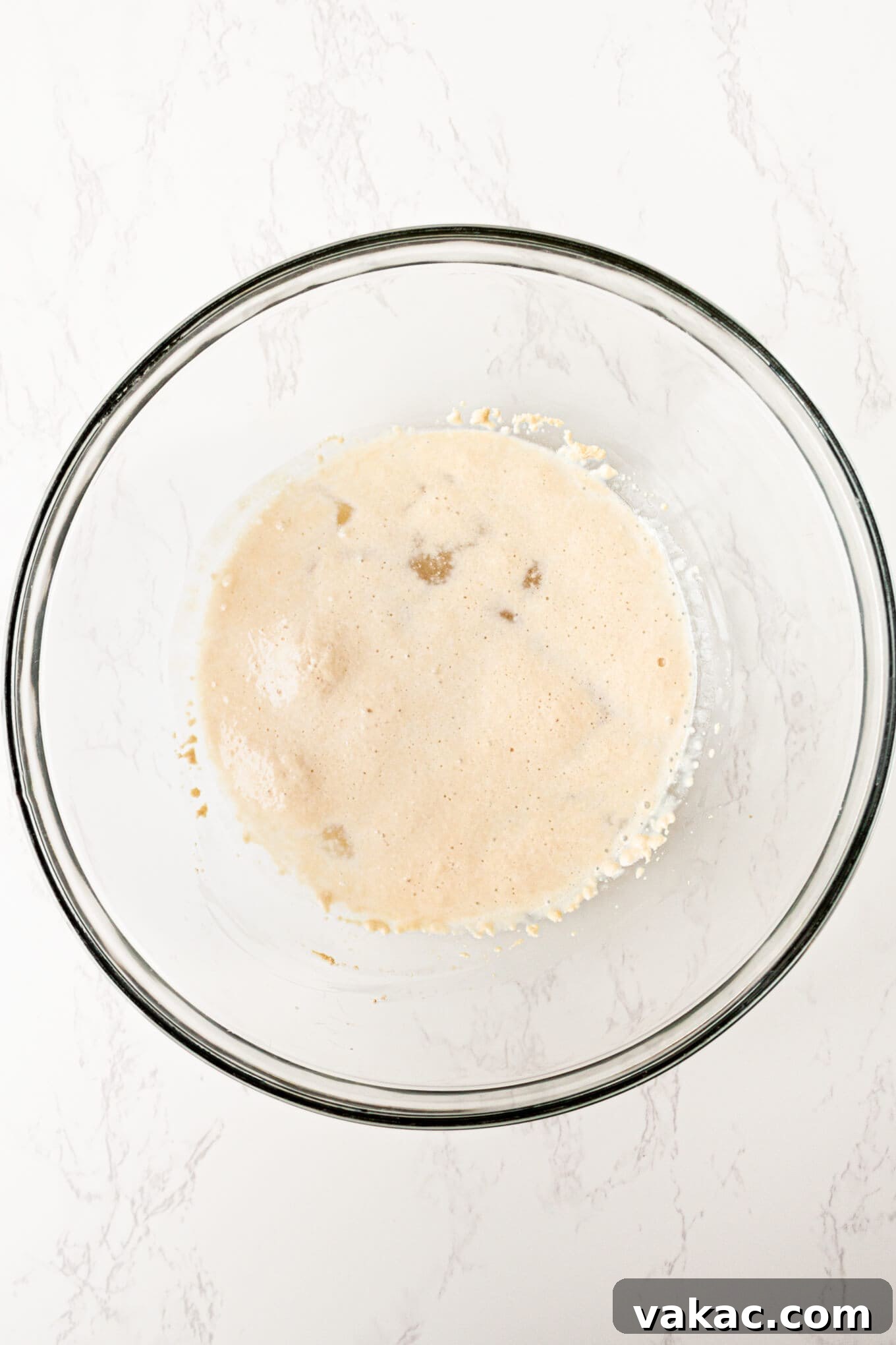 Pillowy Pretzel Gems 4 An overhead shot of active dry yeast proofing in a clear bowl with warm water and sugar, showing a frothy, foamy surface.