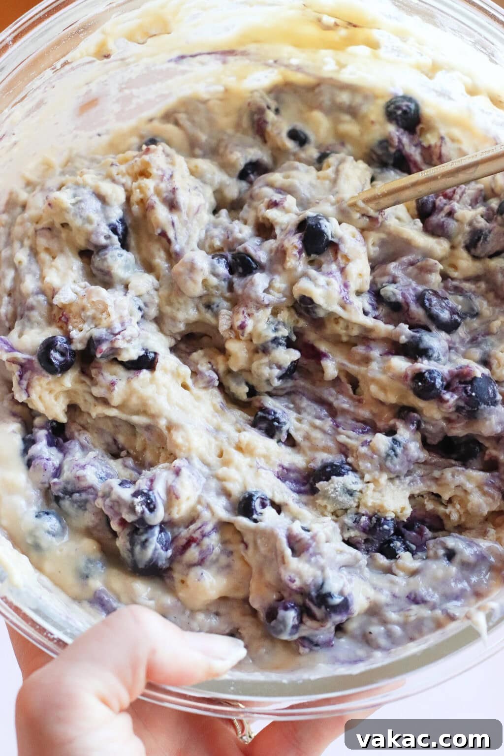 Wholesome Fluffy Blueberry Greek Yogurt Muffins 5g Protein 7 A close-up of a mixing bowl filled with thick blueberry muffin batter being stirred with a spoon, with visible blueberries throughout the mixture.