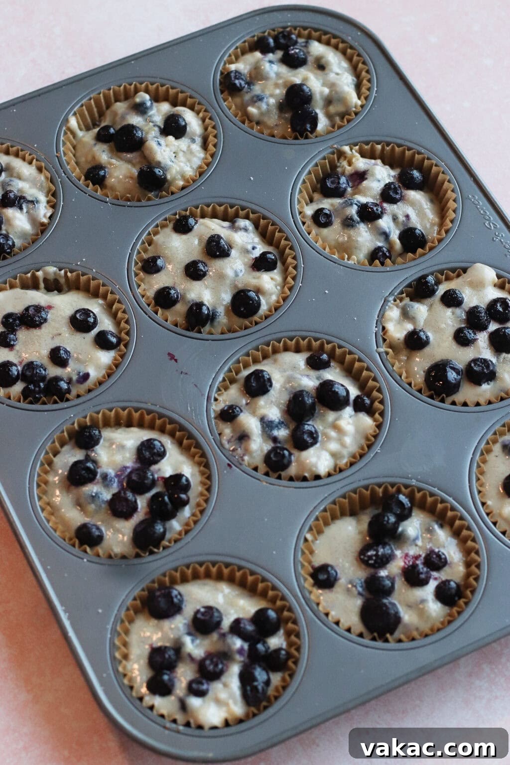Wholesome Fluffy Blueberry Greek Yogurt Muffins 5g Protein 8 A muffin tin filled with paper liners, each holding unbaked blueberry muffin batter topped with fresh blueberries, ready to be baked.