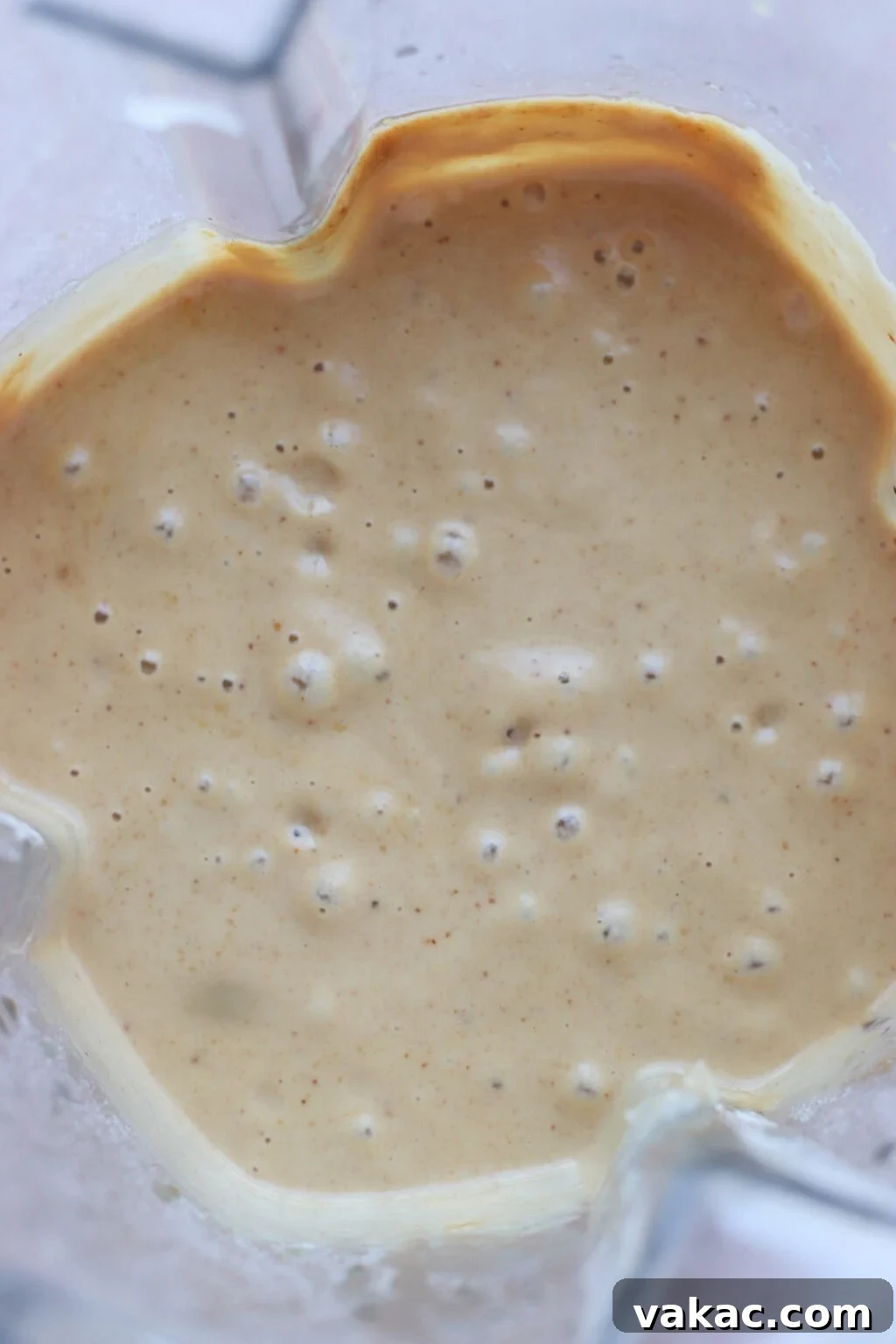 A close-up view of a creamy, light brown batter with small bubbles, seen inside a blender container.