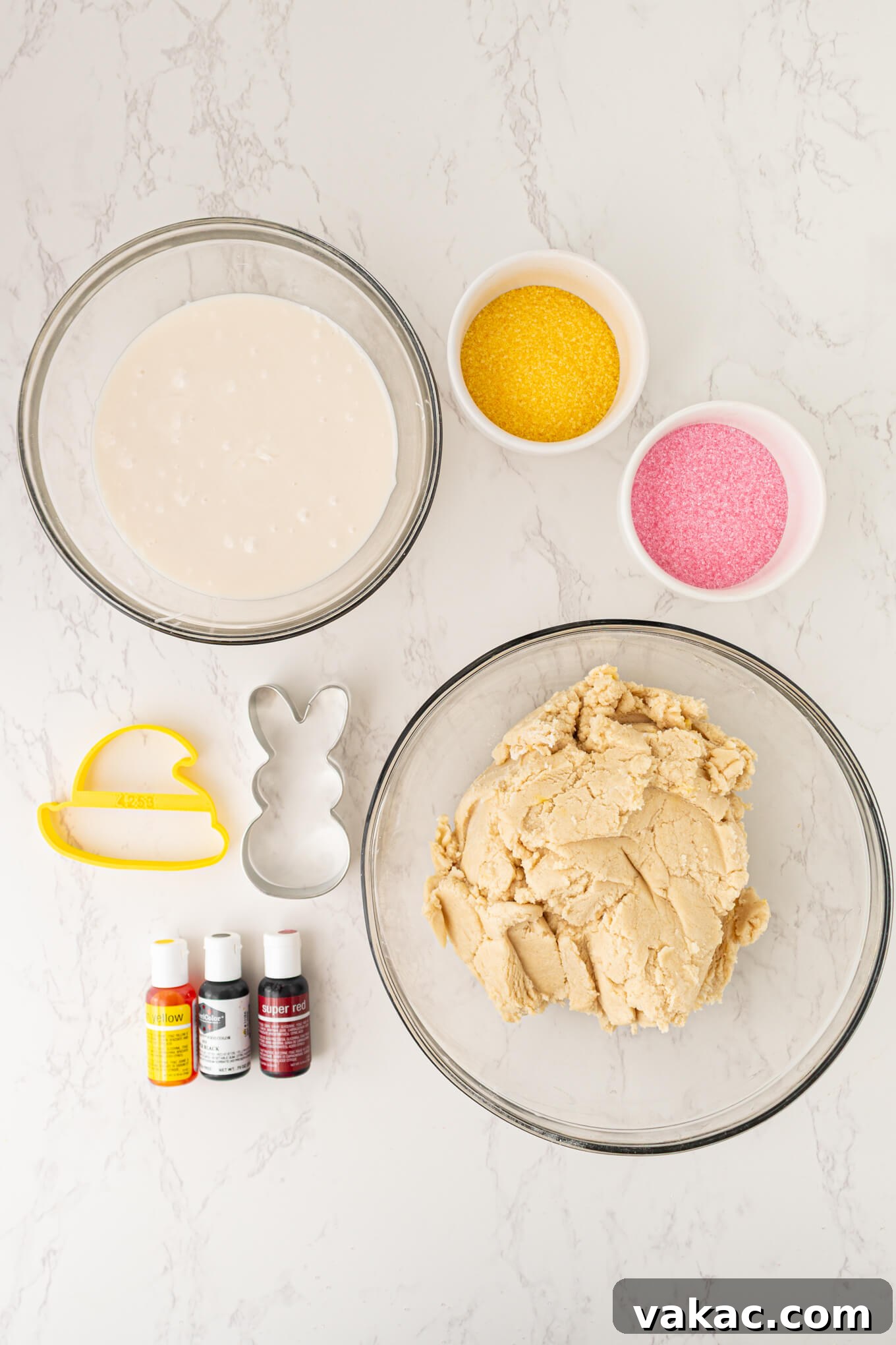 Hoppy Easter Cookies 3 An overhead flat lay of essential ingredients and baking tools, including flour, sugar, an egg, vanilla, cookie cutters, and various food colorings, all neatly arranged for Easter sugar cookie preparation.