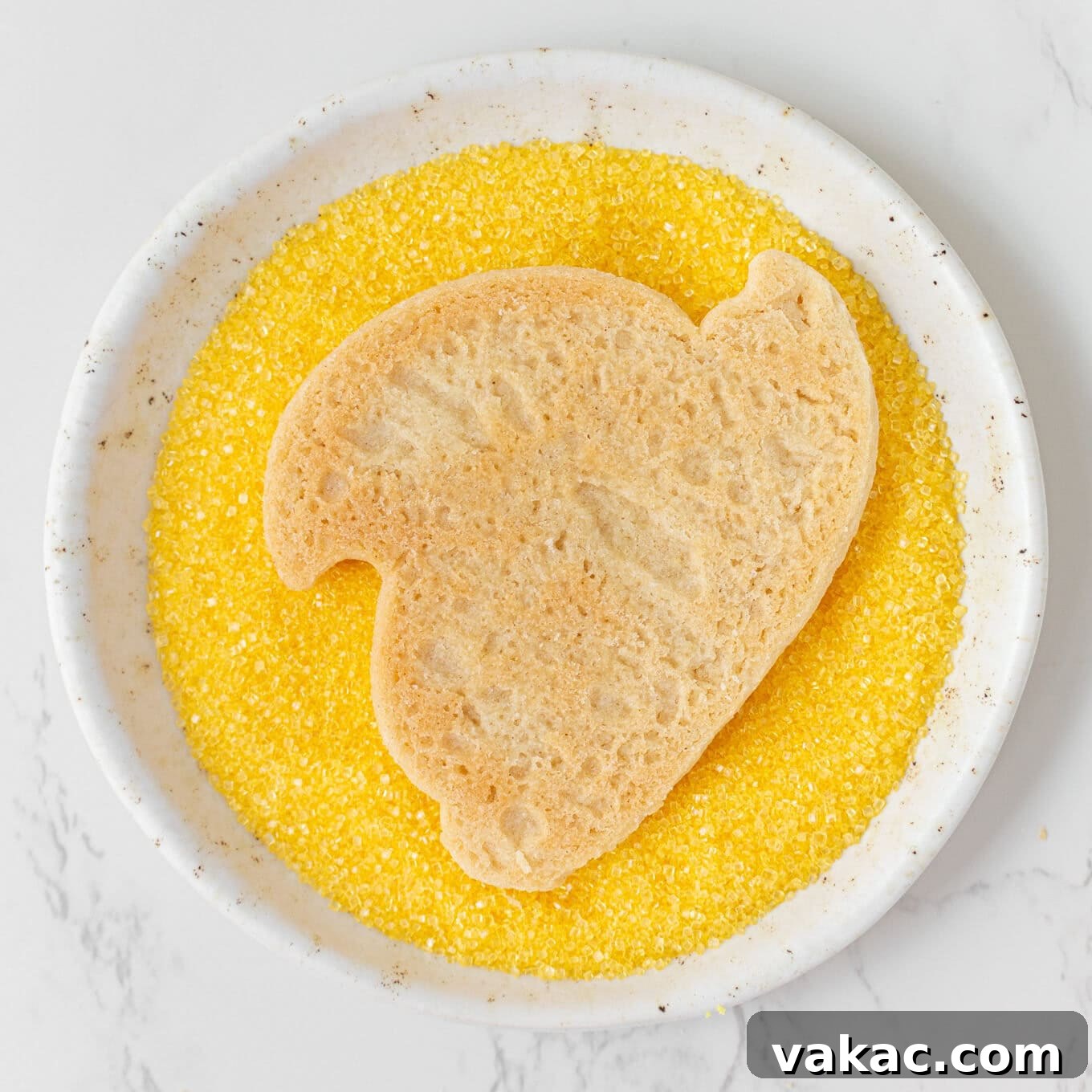 Hoppy Easter Cookies 8 A process shot capturing a chick sugar cookie being gently pressed into a shallow dish filled with sparkling yellow sanding sugar, adhering the sugar to the wet icing.
