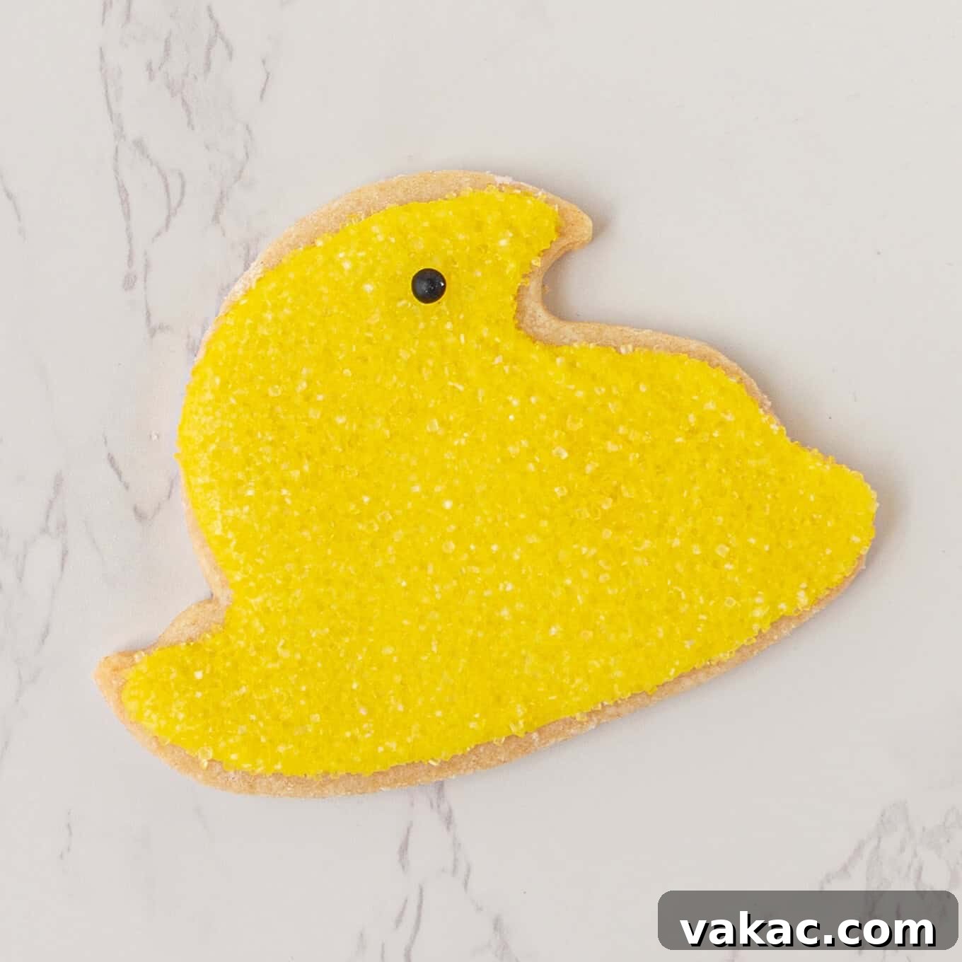 Hoppy Easter Cookies 9 A beautifully decorated baby chick sugar cookie, complete with yellow icing, vibrant sanding sugar, and a small black icing dot for an eye, resting on a wire rack.