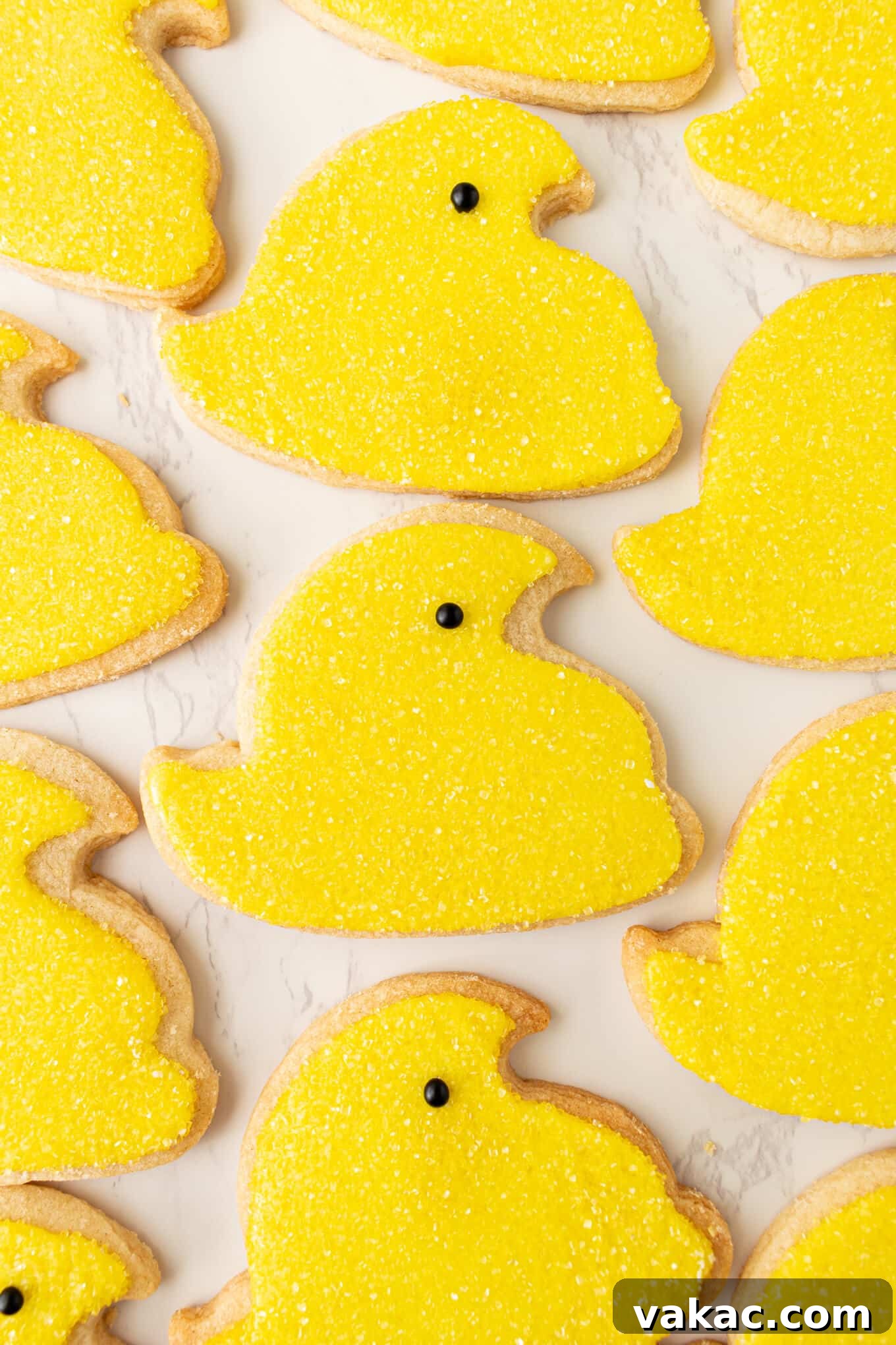 Hoppy Easter Cookies 10 A charming collection of bright yellow chick sugar cookies, meticulously iced and adorned with sparkling yellow sanding sugar and tiny black eyes, arranged neatly.