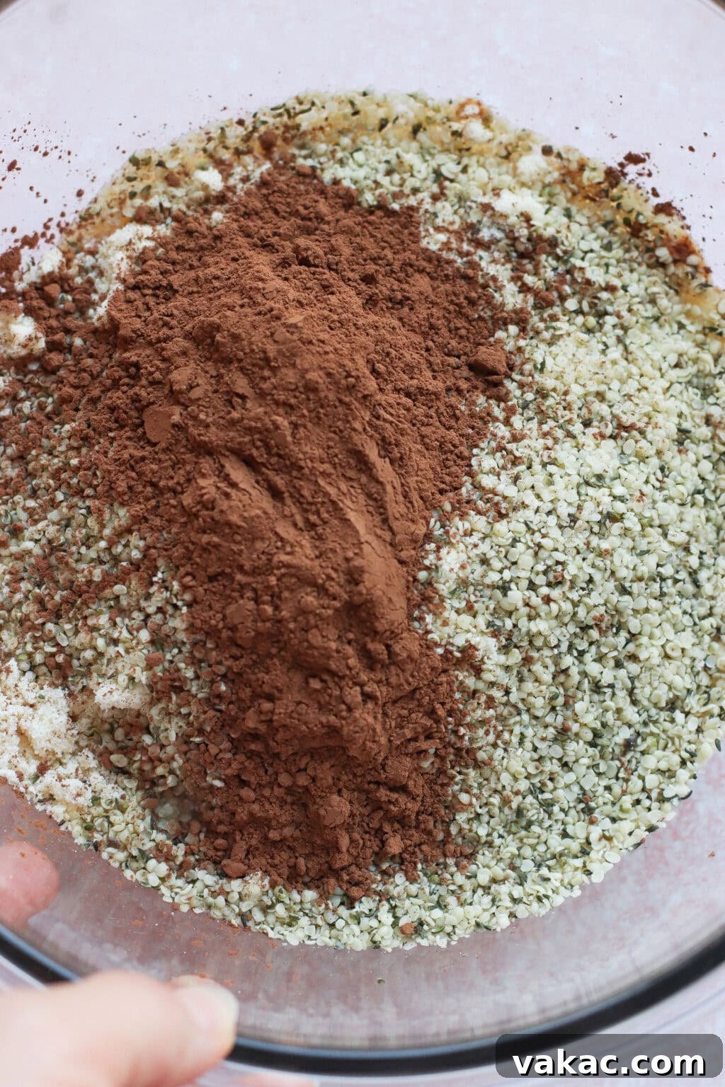 Chocolate Crunch Energy Balls Without Protein Powder 4 A glass bowl filled with a mixture of hemp seeds and a mound of cocoa powder, ready to be mixed for baking or cooking.