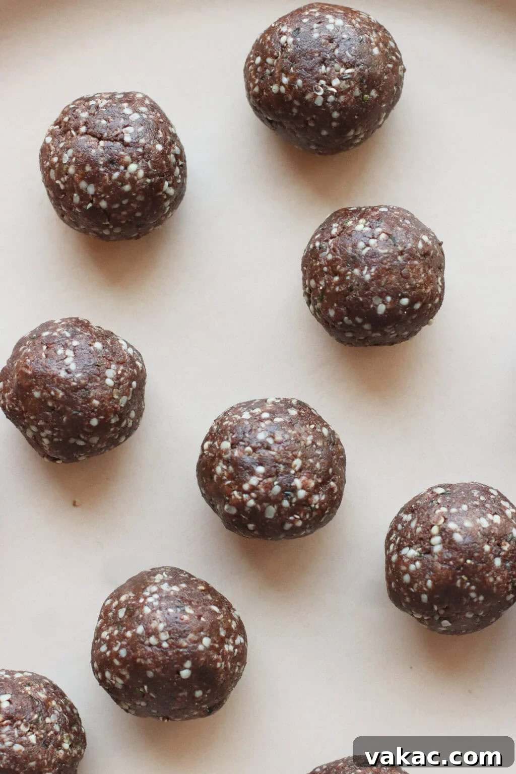 Chocolate Crunch Energy Balls Without Protein Powder 6 Nine chocolate energy balls with visible white seeds are arranged on a light beige surface. The balls have a rough texture and are evenly spaced across the image.