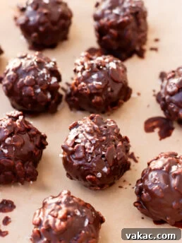 Chocolate-covered crunchy nut clusters arranged on parchment paper, with a glossy coating and a sprinkle of sea salt on top.