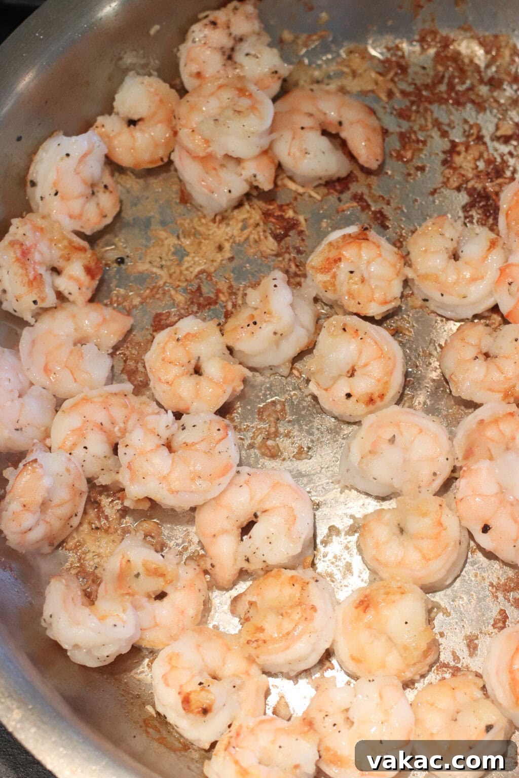 Honey-Soy Shrimp Lettuce Wraps with Crunchy Veggies 5 Shrimp being sautéed in a stainless steel pan; some pieces are lightly browned while others are cooking, with seasoning visible on the shrimp.