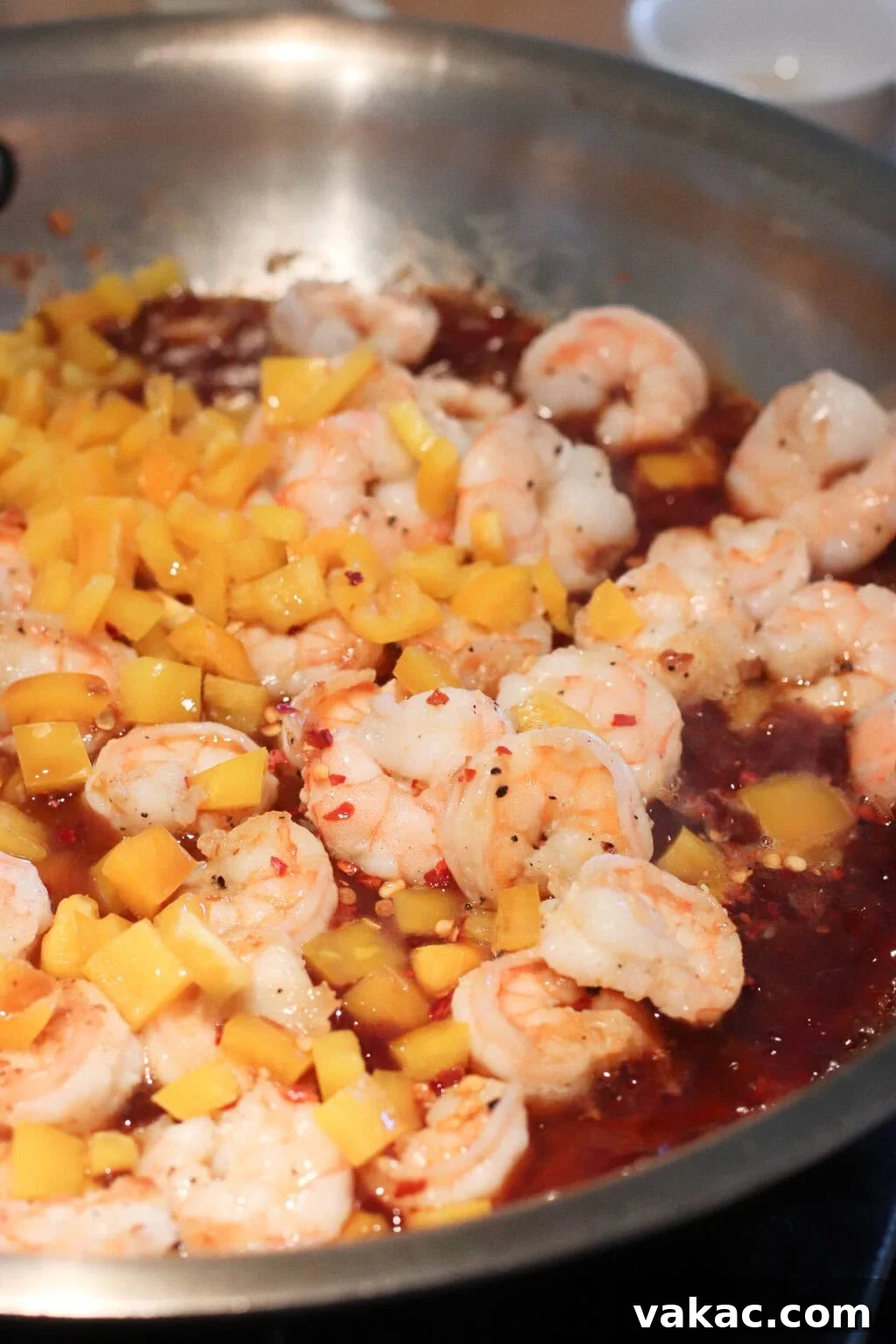 Honey-Soy Shrimp Lettuce Wraps with Crunchy Veggies 7 Shrimp cooking in a pan with diced yellow bell peppers and a reddish sauce, likely being sautéed or stir-fried.