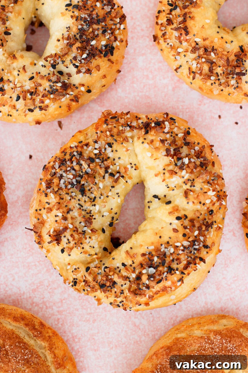 High-Protein Cottage Cheese Bagels Recipe for Homemade Bagels 2 A close-up of several everything bagels on a pink surface, topped with a mix of seeds and seasonings. The bagels are golden-brown and have a rough, homemade texture.