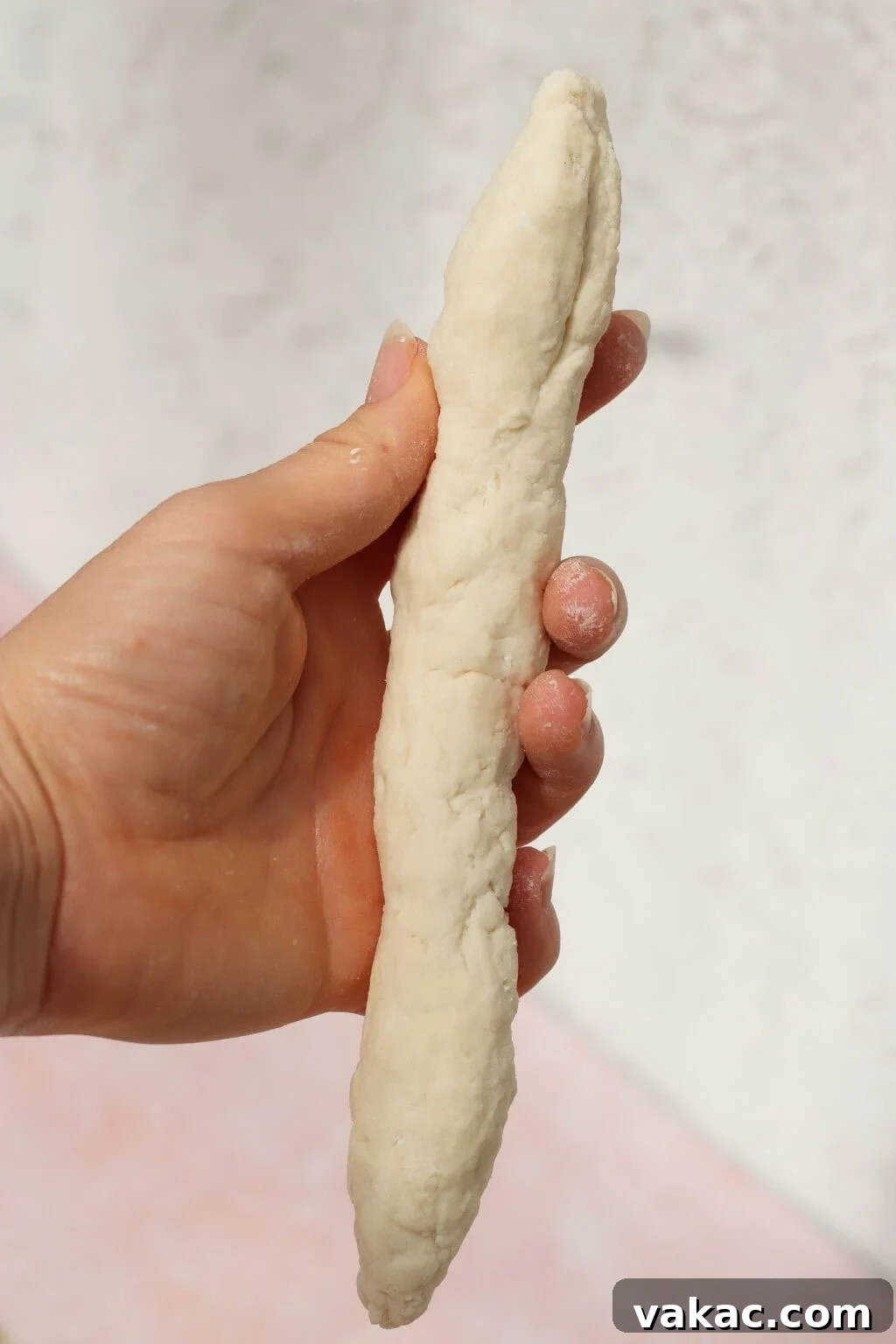 High-Protein Cottage Cheese Bagels Recipe for Homemade Bagels 7 A hand holding a long, slightly uneven piece of raw dough against a light background.