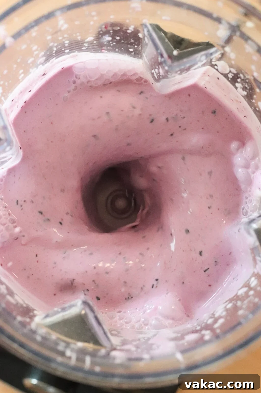 High-Protein Blueberry Chia Pudding (Blended for Creaminess) 5 Close-up view of a blender mixing a creamy, light pink smoothie with small dark specks, creating a swirling vortex in the center.