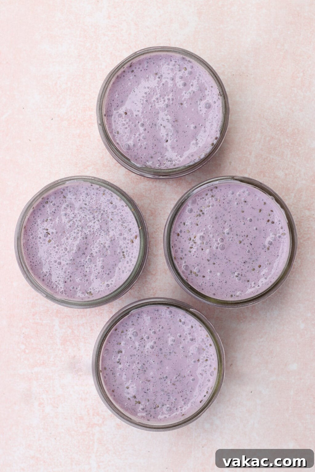 High-Protein Blueberry Chia Pudding (Blended for Creaminess) 6 Four glass jars filled with creamy purple smoothies are arranged on a light pink textured surface.