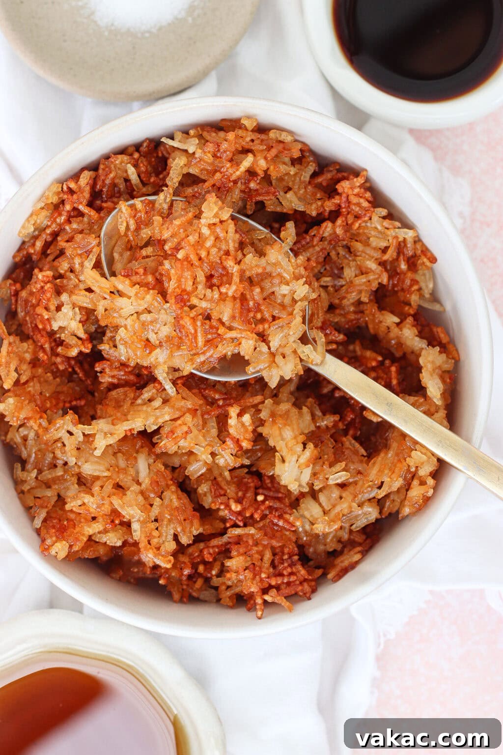 Crispy Sheet Pan Rice for Salads, Bowls and Toppings 4 A bowl of crispy, browned fried rice with a spoon scooping some out. Small dishes of soy sauce and salt are placed nearby on a white cloth.