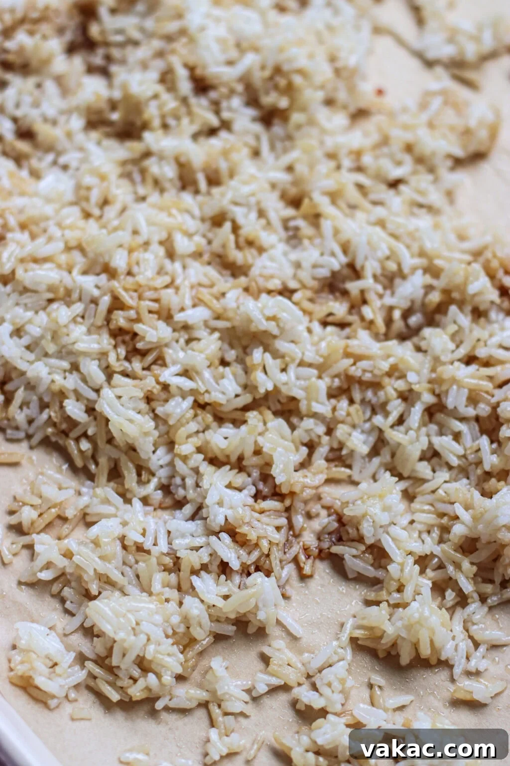 Crispy Sheet Pan Rice for Salads, Bowls and Toppings 5 Cooked white rice spread out on a flat surface, with some grains showing a light brown, toasted color. The rice appears separated and slightly uneven in texture.