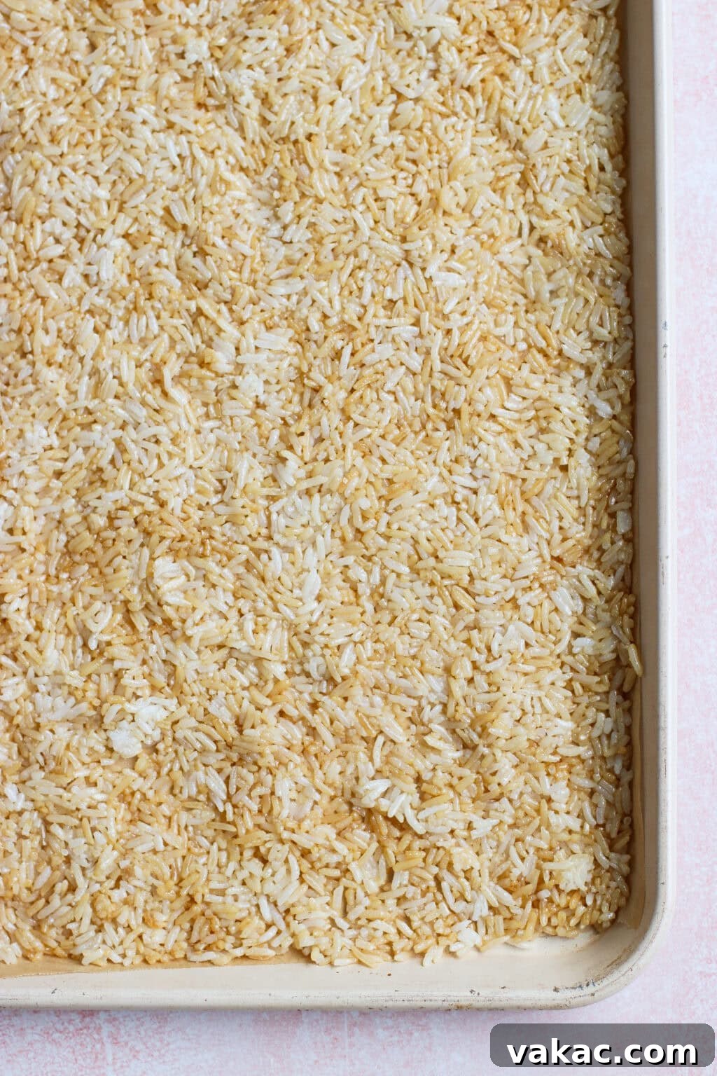 Crispy Sheet Pan Rice for Salads, Bowls and Toppings 6 Uncooked white rice spread evenly on a large rimmed baking sheet, showing a mix of light and slightly toasted grains.
