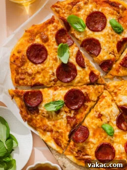 Pepperoni pizza sliced on a wooden board, topped with fresh basil leaves. A glass of drink and a bowl of fresh basil leaves are nearby.
