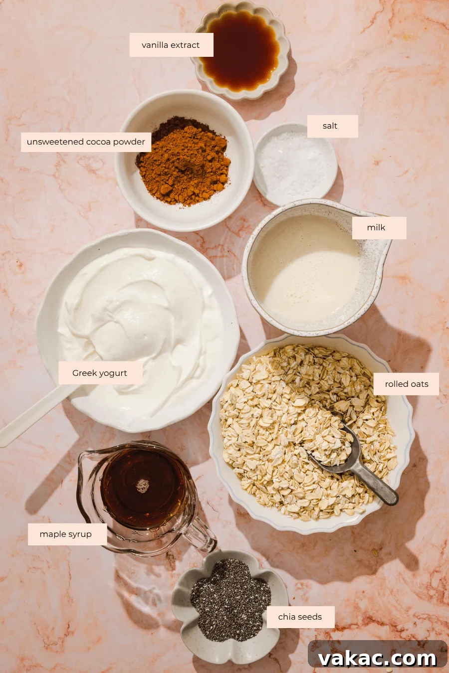 Protein-Packed Chocolate Overnight Oats with Greek Yogurt 4 Bowls of Greek yogurt, unsweetened cocoa powder, salt, milk, rolled oats, maple syrup, chia seeds, and vanilla extract are arranged on a marble surface, each ingredient labeled with text.